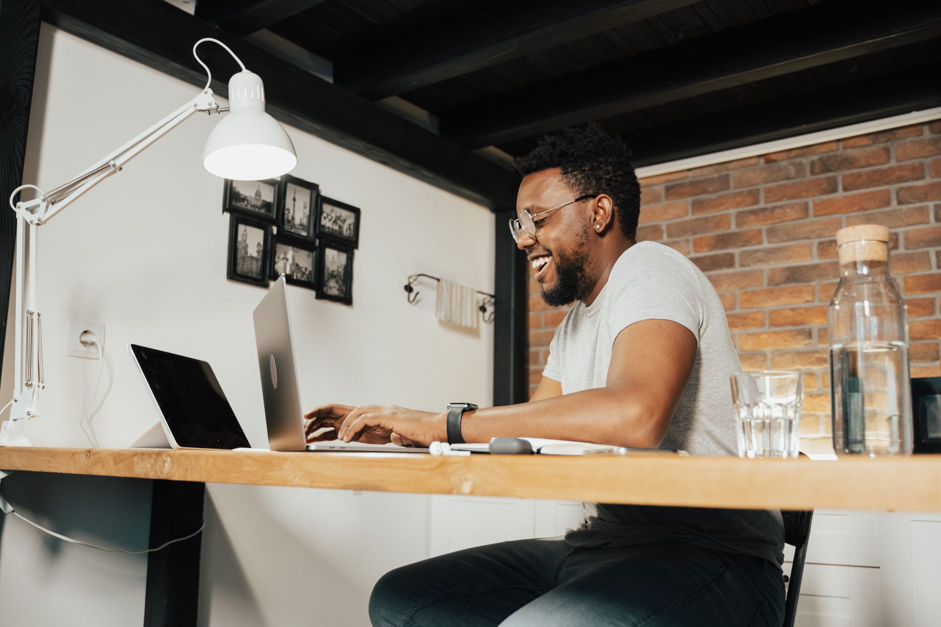 A man smiling while typing on a laptop at a home office desk.